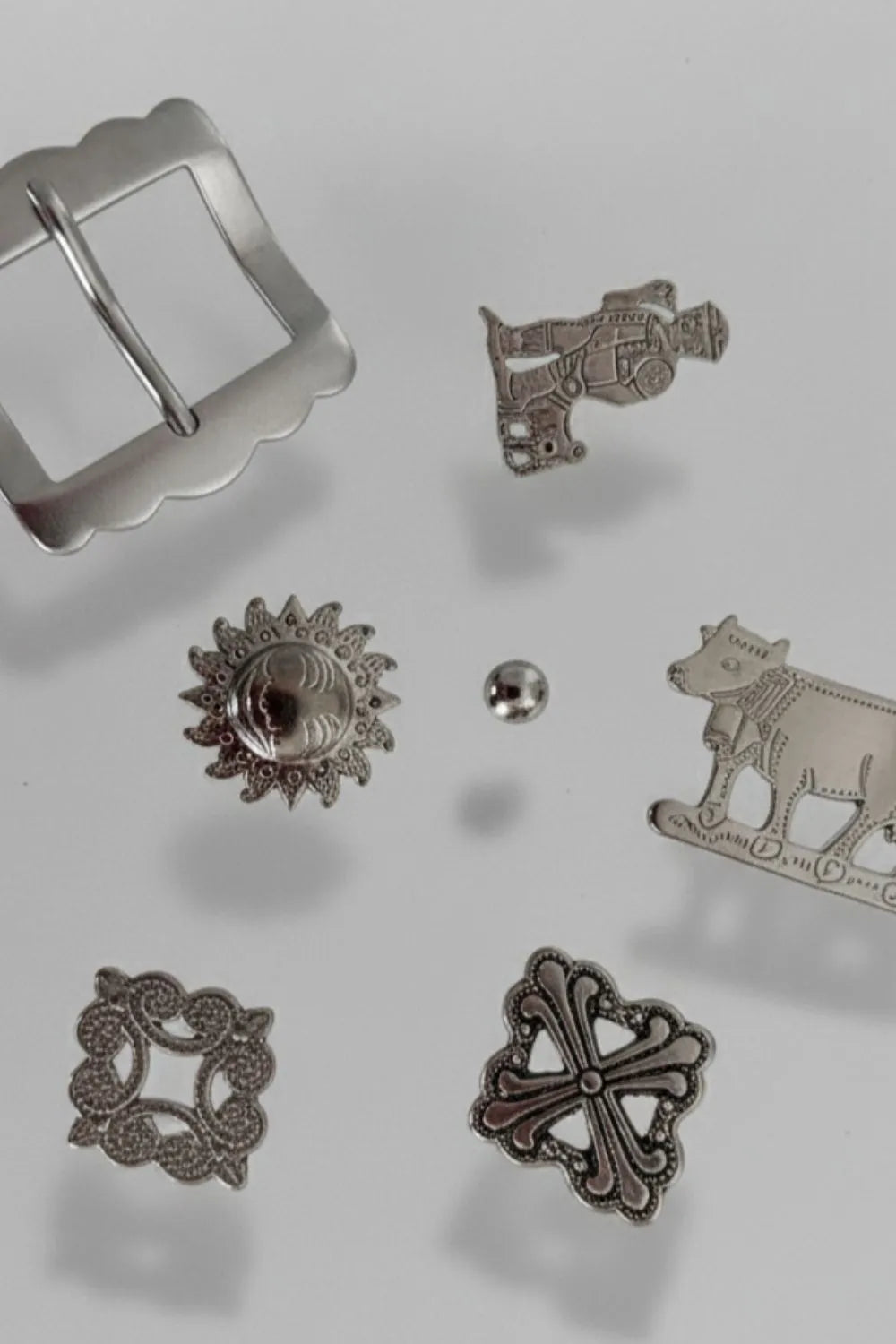 Detailaufnahme traditioneller Metallbeschläge für Appenzeller Gürtel von Edelvetica, darunter Edelweiss-Ornamente, Kuhmotive und Schnallen aus hochwertigem Metall