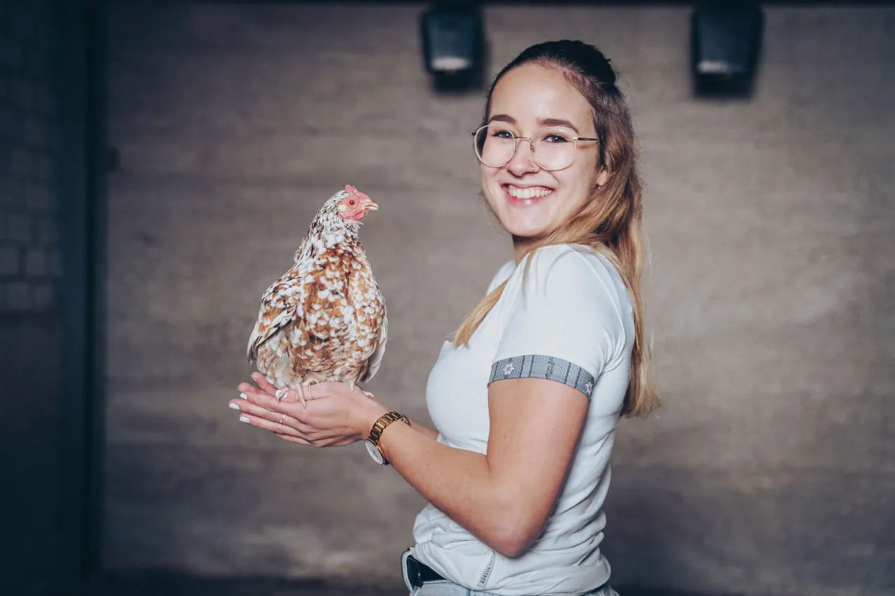 Huhn sitz in der Hand einer Frau die ein Edelvetica Shirt trägt